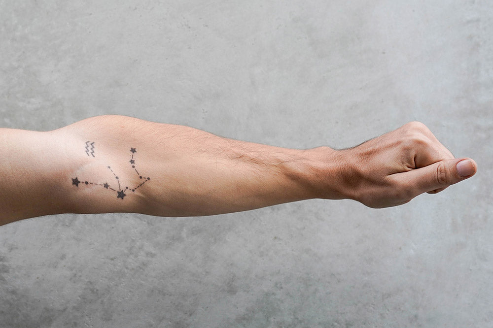 A forearm with a temporary tattoo showing an Aquarius zodiac constellation and small wave-like symbols