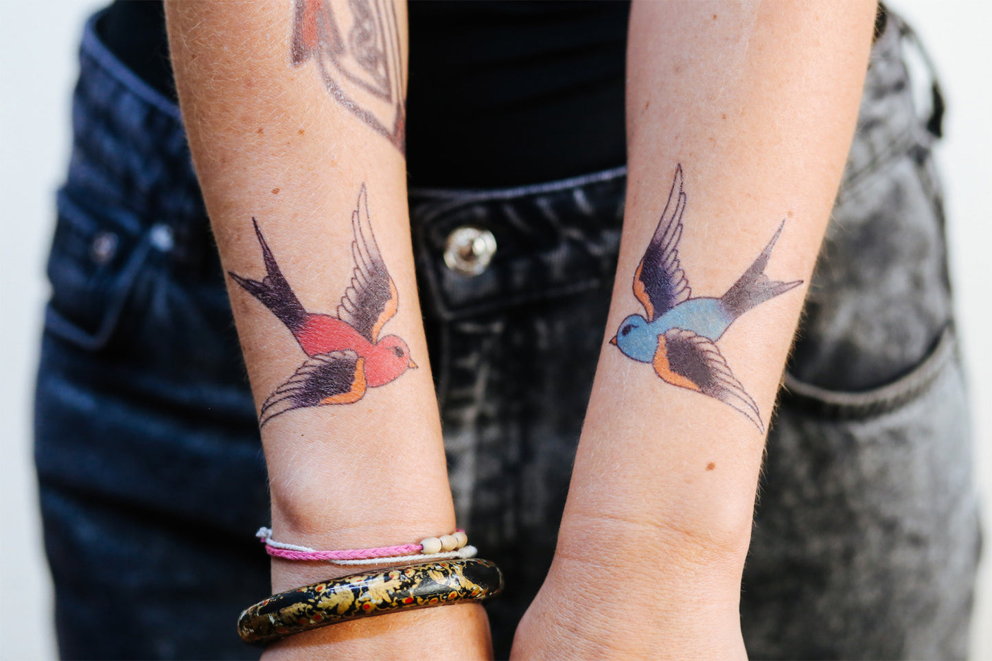 Two forearms with tattoos of blue and red swallows