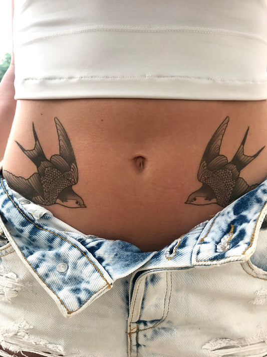 Realistic black swallows tattoo on a person's lower abdomen