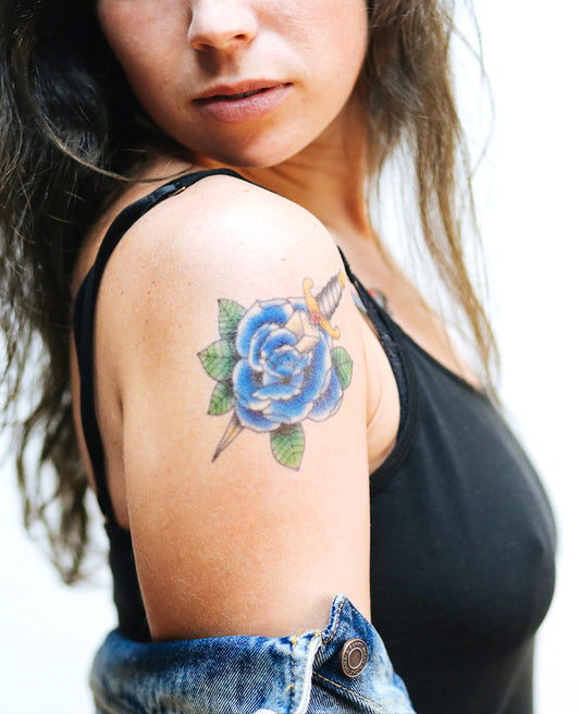 Realistic blue rose and dagger tattoo on a person’s upper arm